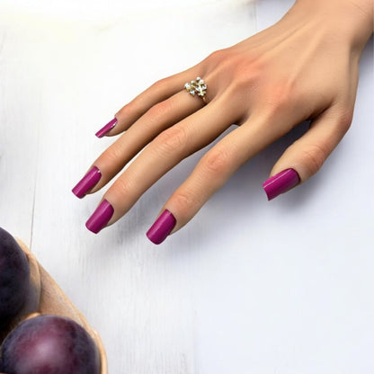 Ongles violet Plum Madame Nails sur une table en bois clair avec des prunes sur le côté. 