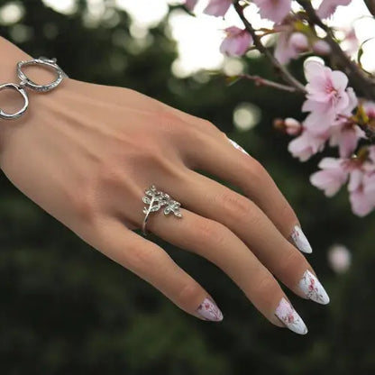 Main manucurée avec des ongles fleuris près d'une branche de cerisier en fleurs