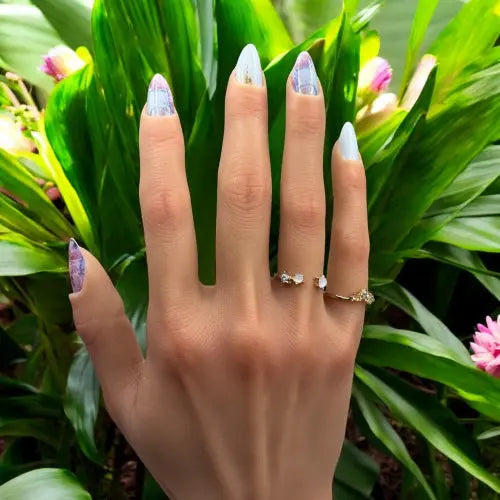 Main avec des ongles portant les nail wraps Floréale posés sur une plante fleurie. 