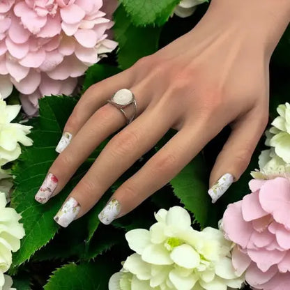 Main manucurée avec des nail wraps Jardin secret entourée d'hortensias clairs. 